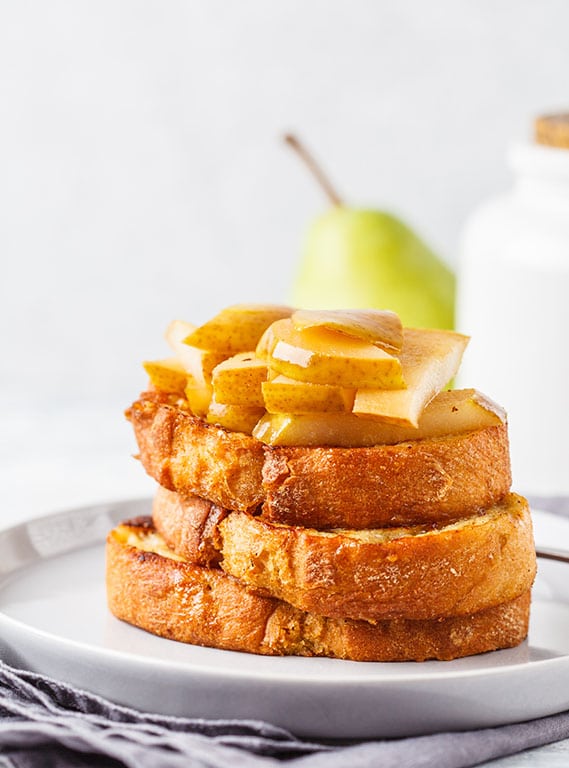 Baked french toast with caramelized pear and syrup on a gray background.