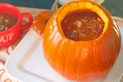 beef stew cooked in a pumpkin looking inside with a bowl of stew sitting next to the pumpkin