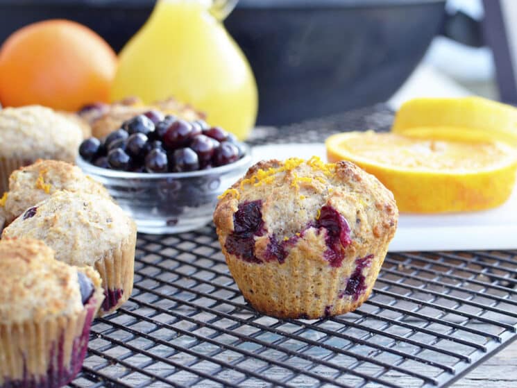 whole wheat orange blueberry muffins on a cooling rack with blueberries and oranges in the background