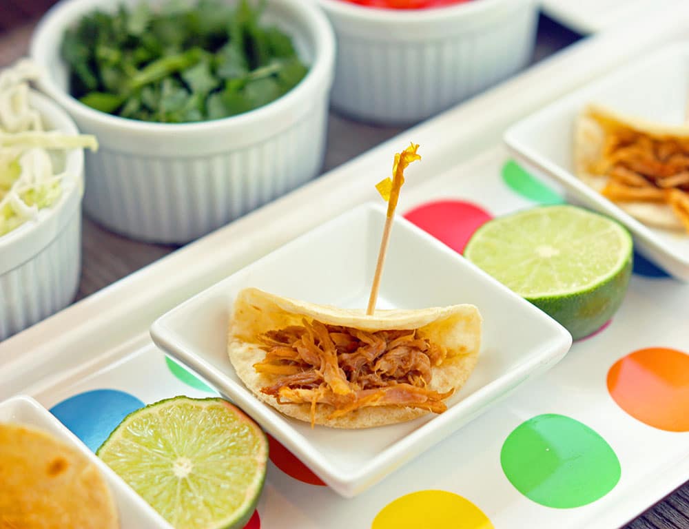 slow cooker honey lime pork tacos on a plate and a polka dot tray underneath