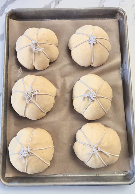 sourdough bread bowl dough with twine tied to create a pumpkin shape on a baking sheet