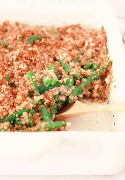 green bean casserole closeup photo in a white baking dish with a wooden soon