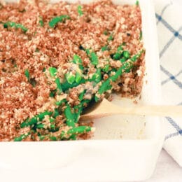 green bean casserole in a white baking dish with a wooden spoon serving some