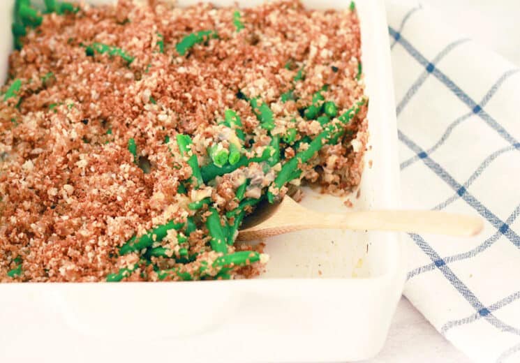 green bean casserole in a white baking dish with a wooden spoon serving some