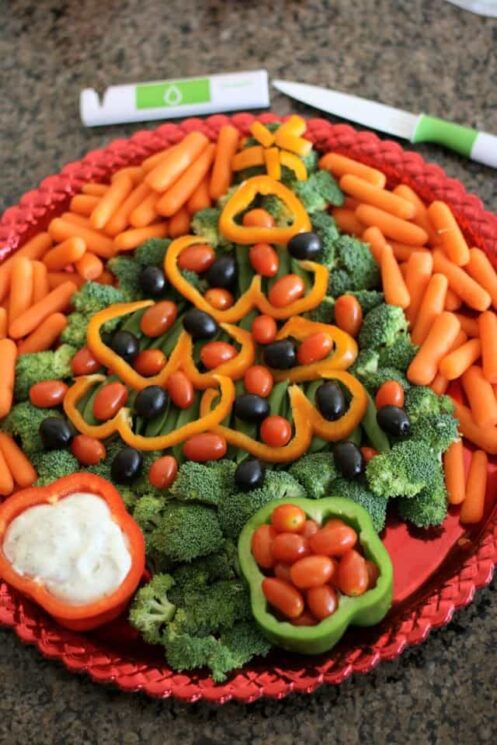 Christmas tree made with broccoli, bell peppers, olives and tomatoes with a bell pepper as a dip bowl on a red platter