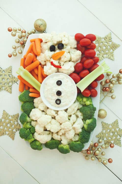 Cauliflower snowman surrounded by broccoli, carrots and tomatoes on a christmas background