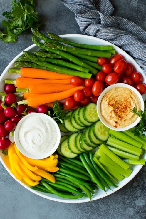 White platter with assorted veggies and different dips in white bowls