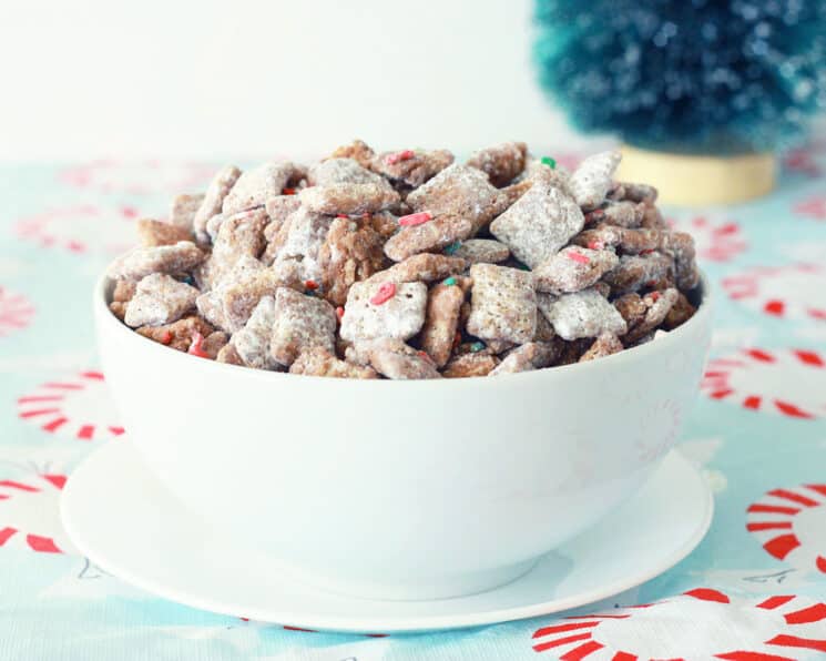 cereal coated in a chocolate, powdered sugar and holiday sprinkles in a white bowl on a candy cane tablecloth