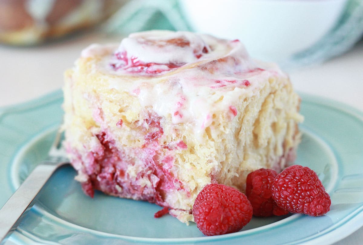 raspberry whole wheat sweet roll on a blue plate with fresh raspberries on the plate