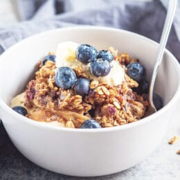 Oatmeal baked with blueberries in a white bowl with a spoon, blueberries and yogurt on top