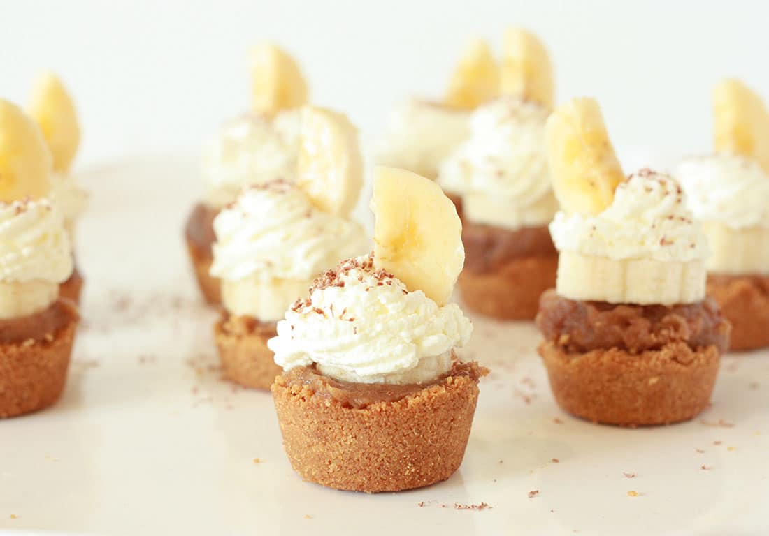 banoffee pie bites with whip cream and a sliced banana on top on a white plate