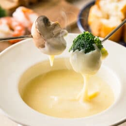 cheese fondue in a white bowl with a mushroom and broccoli