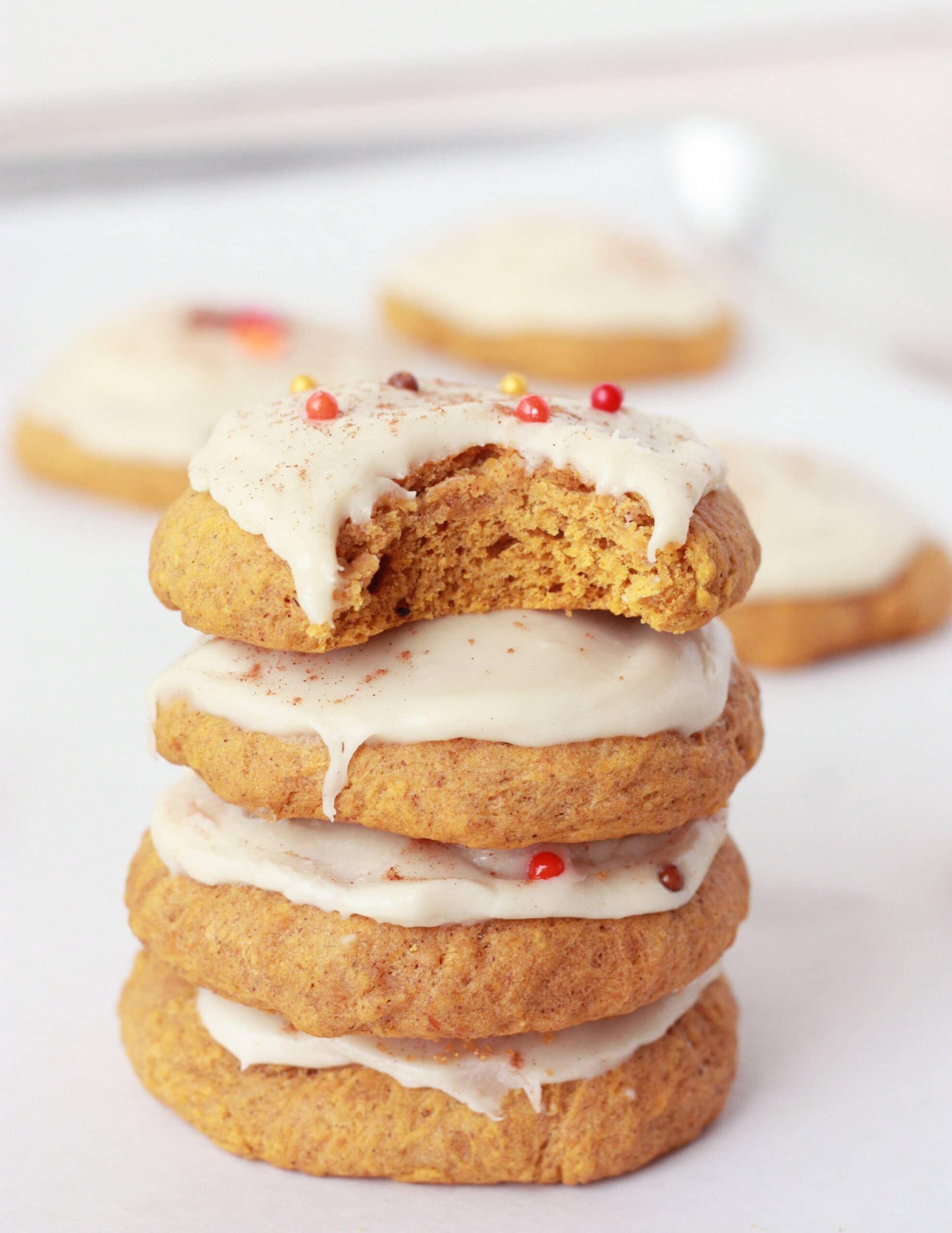 soft pumpkin cookies in a stack with frosting and sprinkles