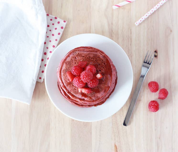 Stack of dye-free pink pancakes on a plate with raspberries and strawberries from above - top view