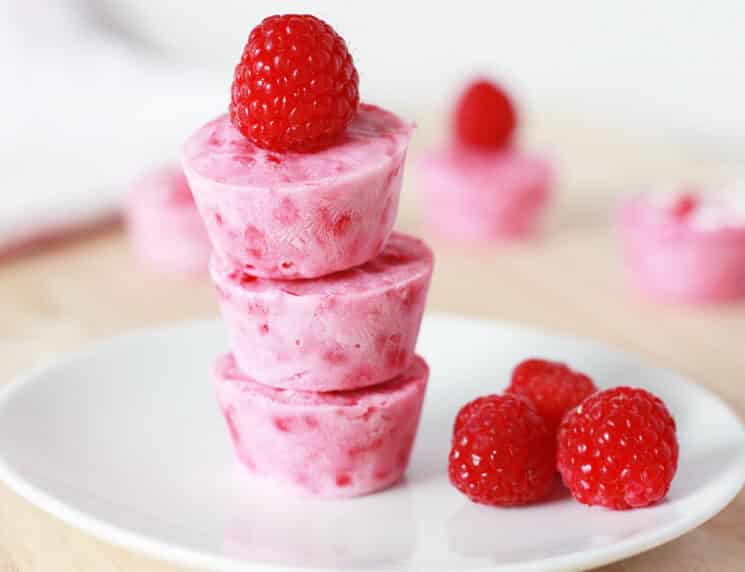 three raspberry frozen yogurt bites stacked and topped with fresh raspberries