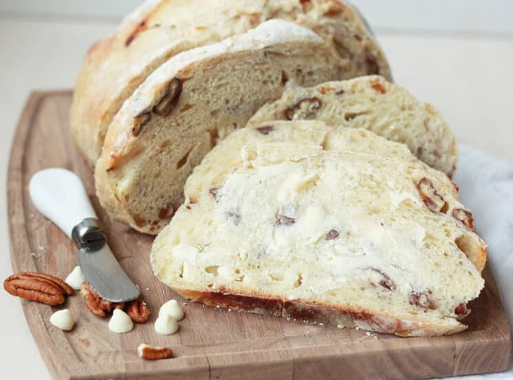 sliced ​​loaf of white chocolate pecan sourdough bread on a wooden cutting board and the top slice is buttered