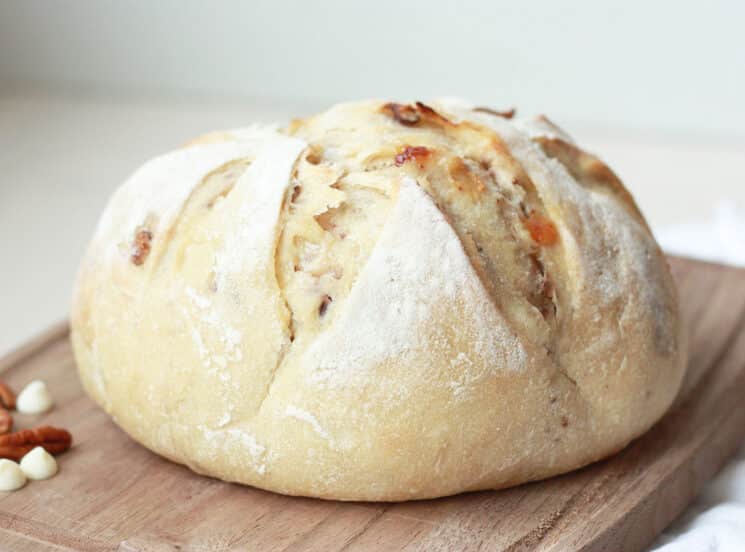 whole loaf of white chocolate pecan sourdough bread sitting on a wooden cutting board