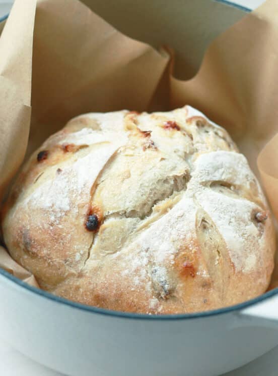 whole loaf of white chocolate pecan sourdough bread in a dutch oven with parchment paper