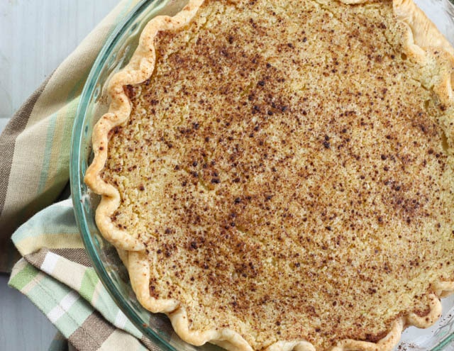 a whole pie topped with cinnamon in a glass pie pan set on a plaid dish towel