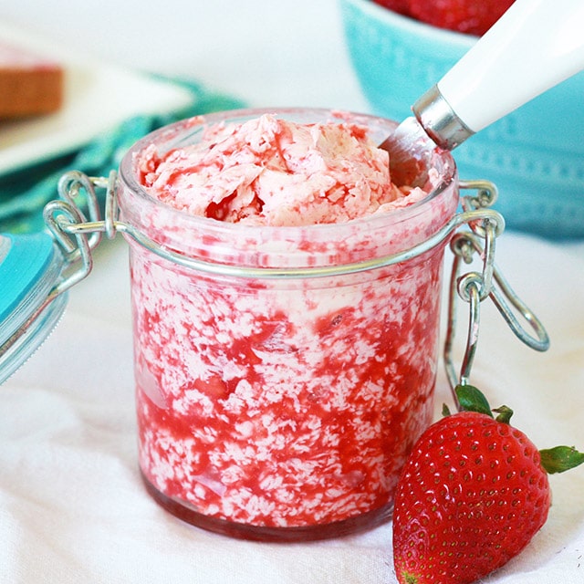 fresh strawberry butter in a glass container with a butter knife and strawberry in front of it
