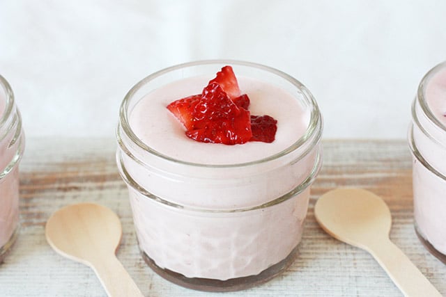 high protein strawberry mousse in small glass jars with chopped strawberries on top and wooden spoons sitting next to the jars