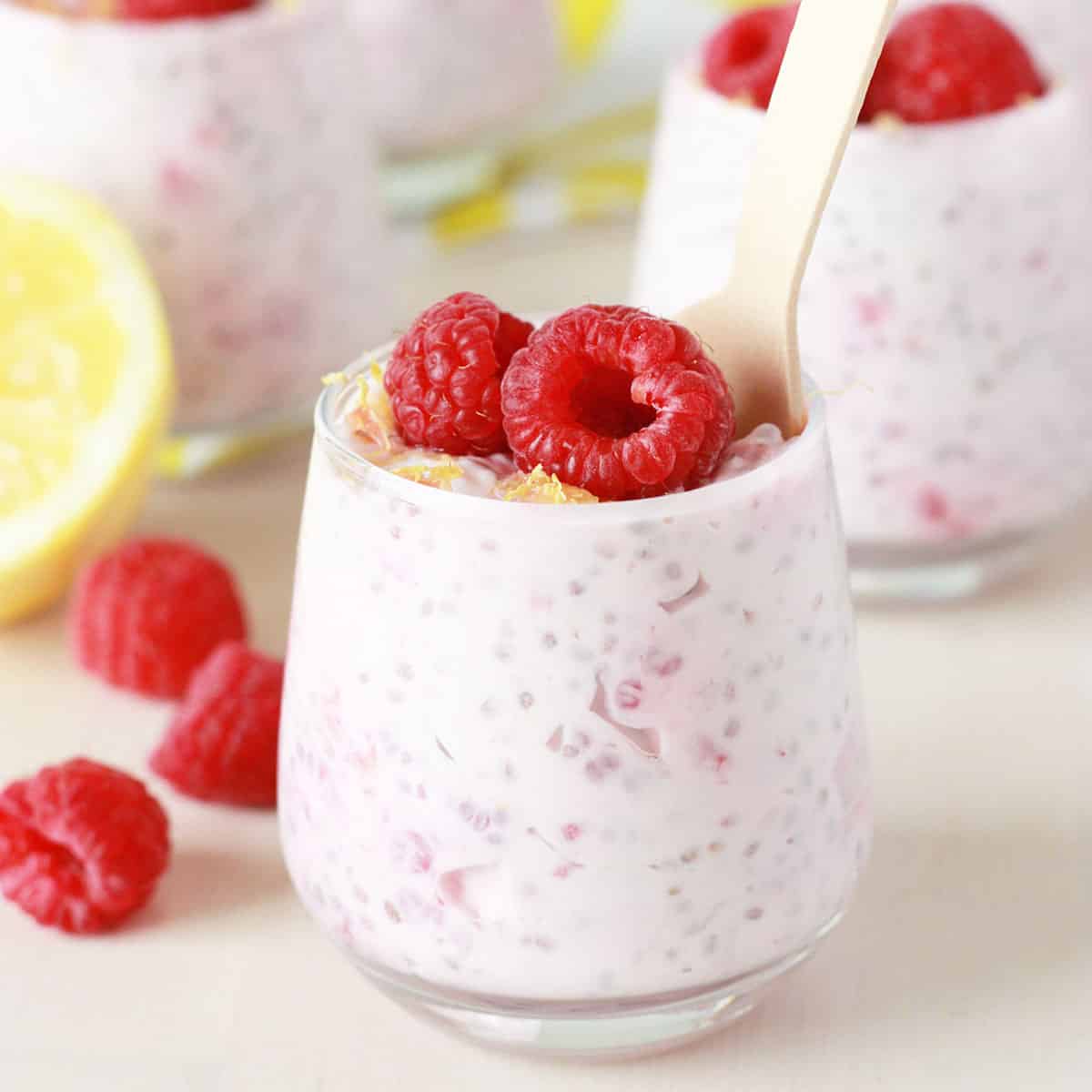 lemon raspberry chia seed pudding in small glass jars with fresh raspberries and lemon zest on top with a small silver spoon in the jar and a fresh lemon in the background