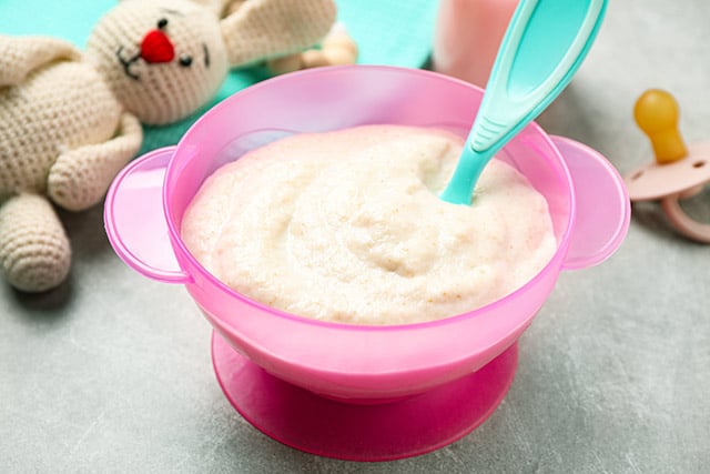 homemade baby cereal from scratch in a pink bowl with a bunny stuffed animal in the background