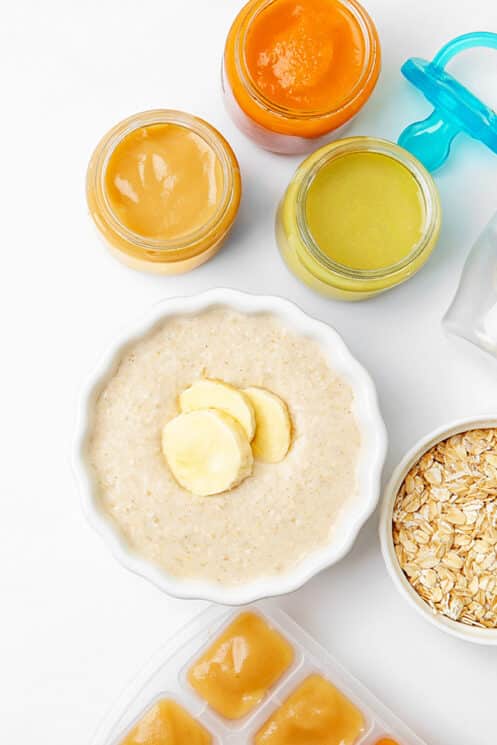 overhead view of homemade baby cereal from scratch with banana slices on top and other baby food in the background