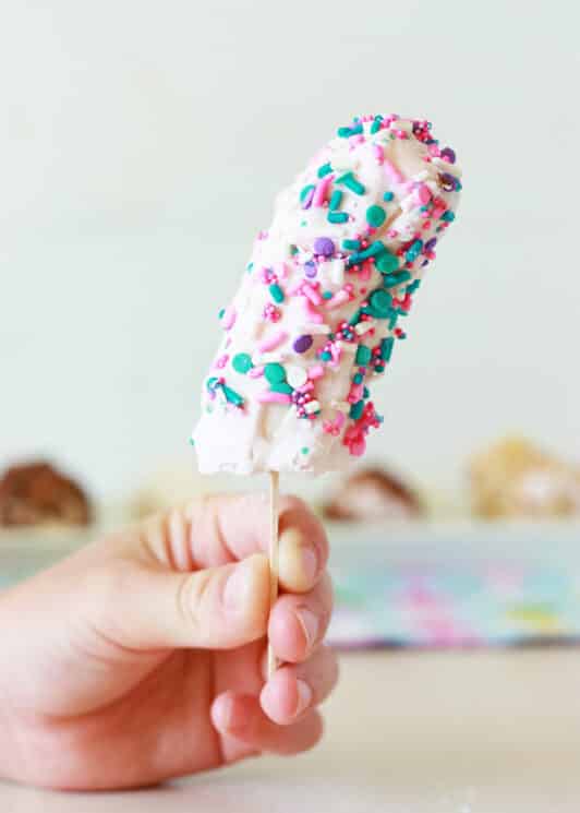 frozen banana pop held by a child covered in yogurt and sprinkles