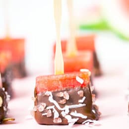 Close up view of watermelon pops with wooden sticks covered with chocolate, coconut and sliced ​​almonds on a pink tray