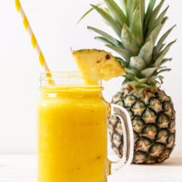 pineapple cooler in a glass jar with a handle with a striped straw and a pineapple in the background