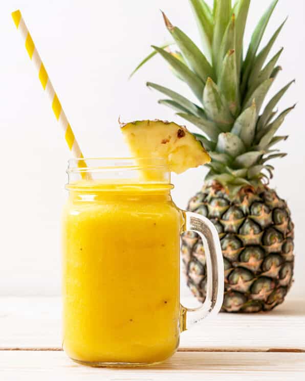 pineapple cooler in a glass jar with a handle with a striped straw and a pineapple in the background