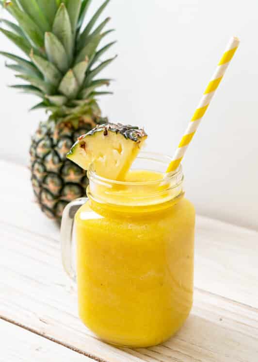 pineapple cooler in a glass jar with a handle with a striped straw and a pineapple in the background