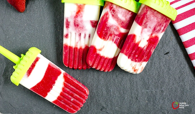 Top view of strawberry creamsicles on dark background with green popsicle sticks