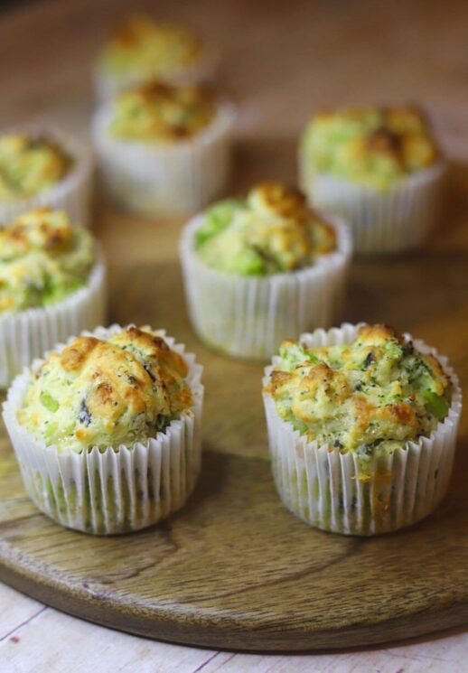 broccoli and cheese muffins in white paper liners on a wooden table