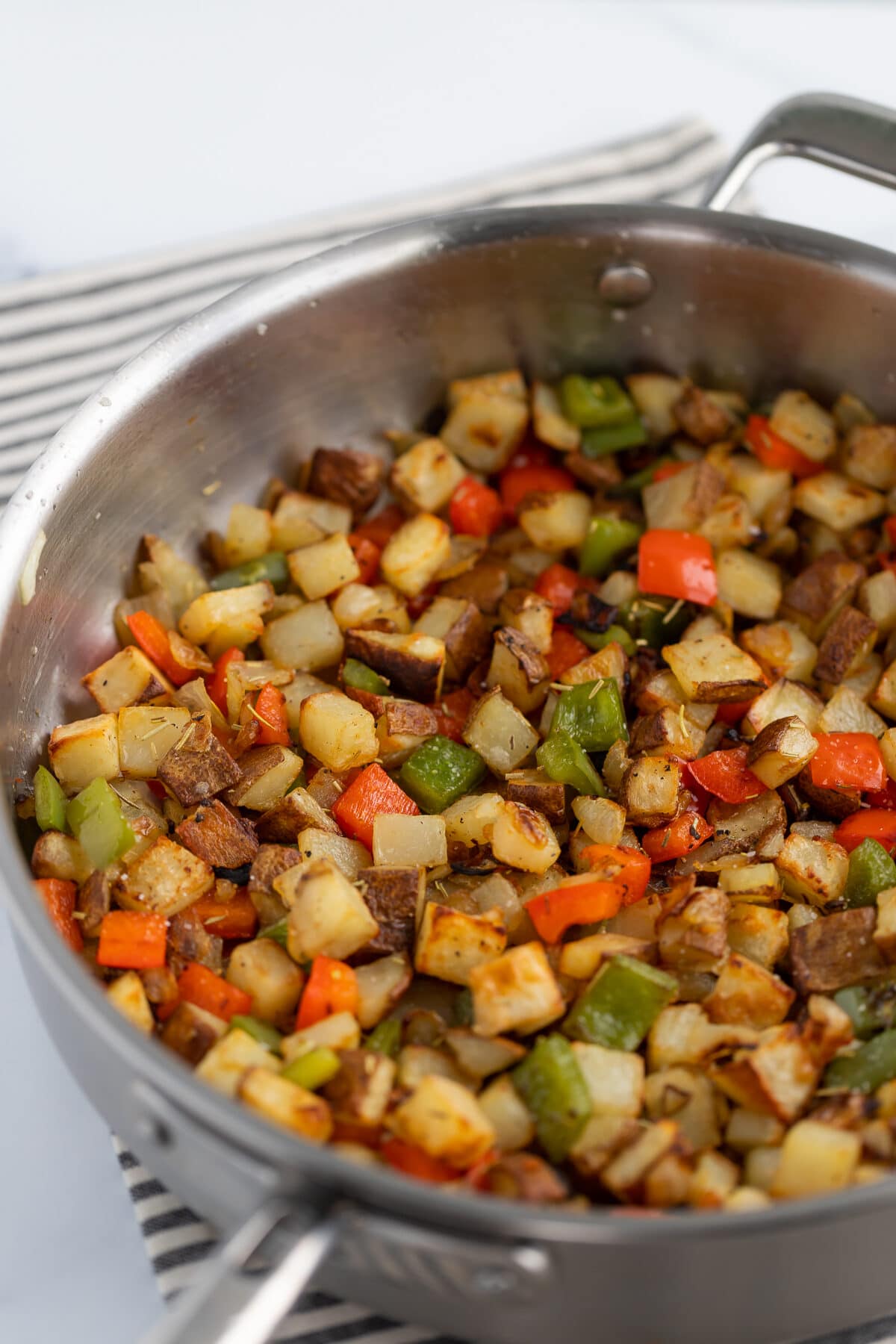 skillet potatoes with red bell peppers and onions in a stainless steel skillet