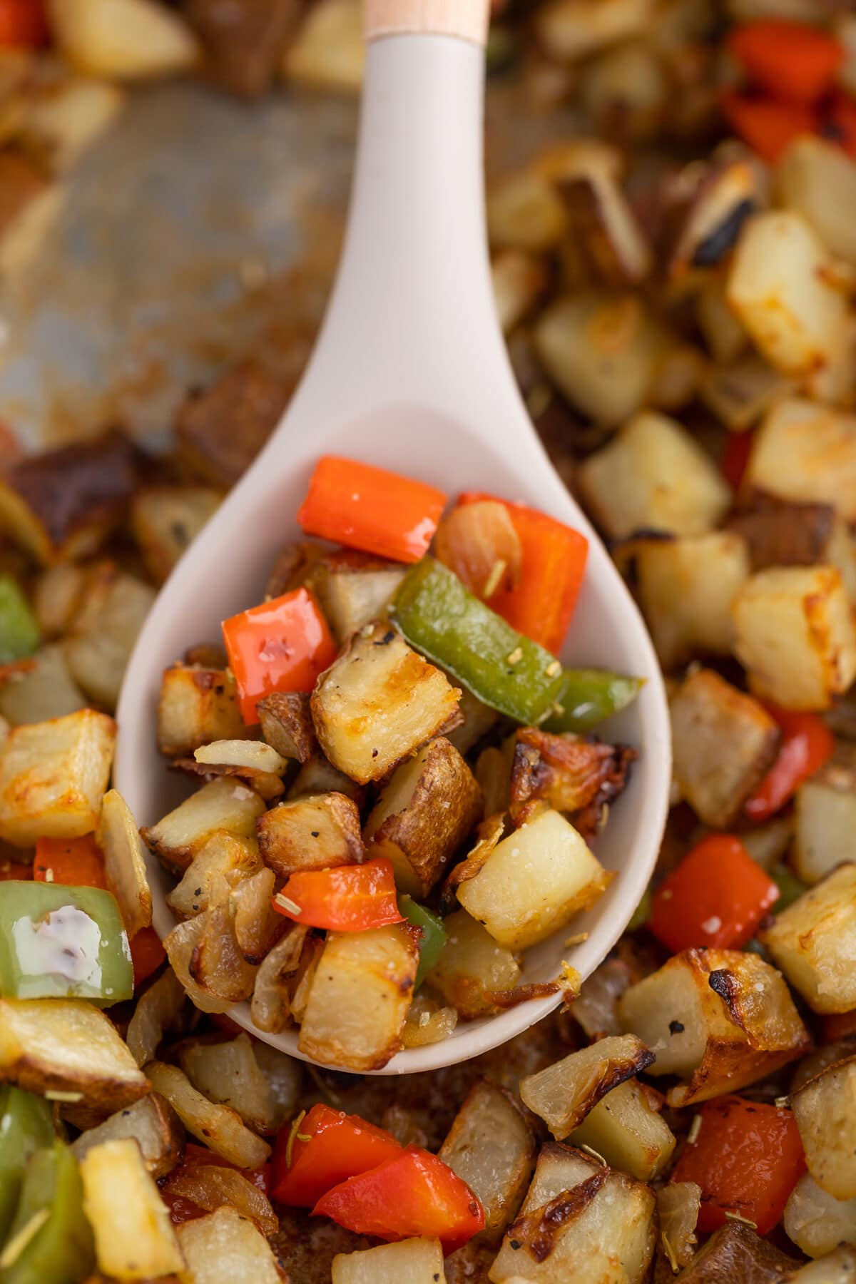 crispy skillet potatoes with bell peppers and  onions close up on a serving spoon