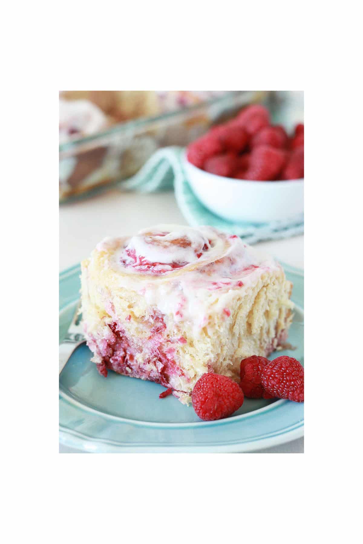 single raspberry roll on a blue plate in front of a dish of raspberry rolls