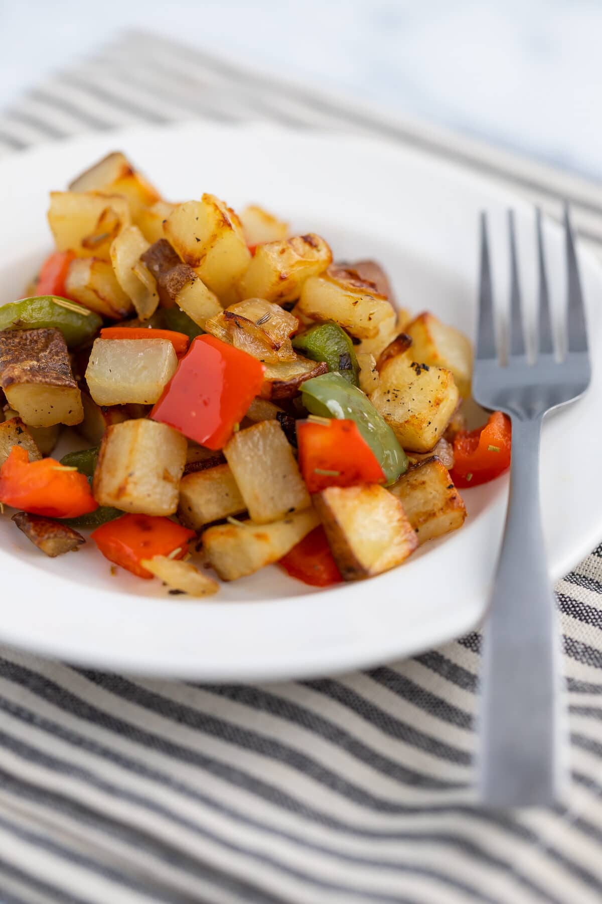 skillet potatoes with sweet peppers in a white bowl with a fork