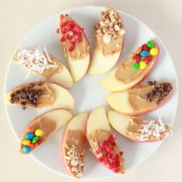 apple wedge snack with toppings and peanut butter on a white circle plate