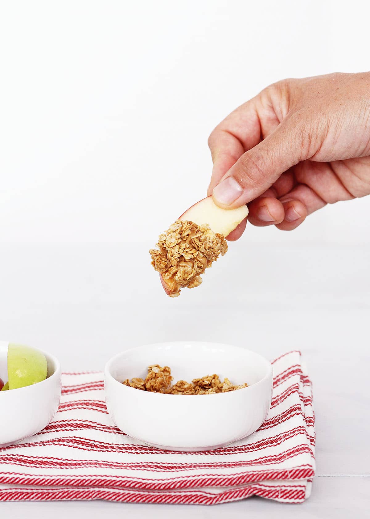 dipping an apple wedge with peanut butter into a bowl of granola