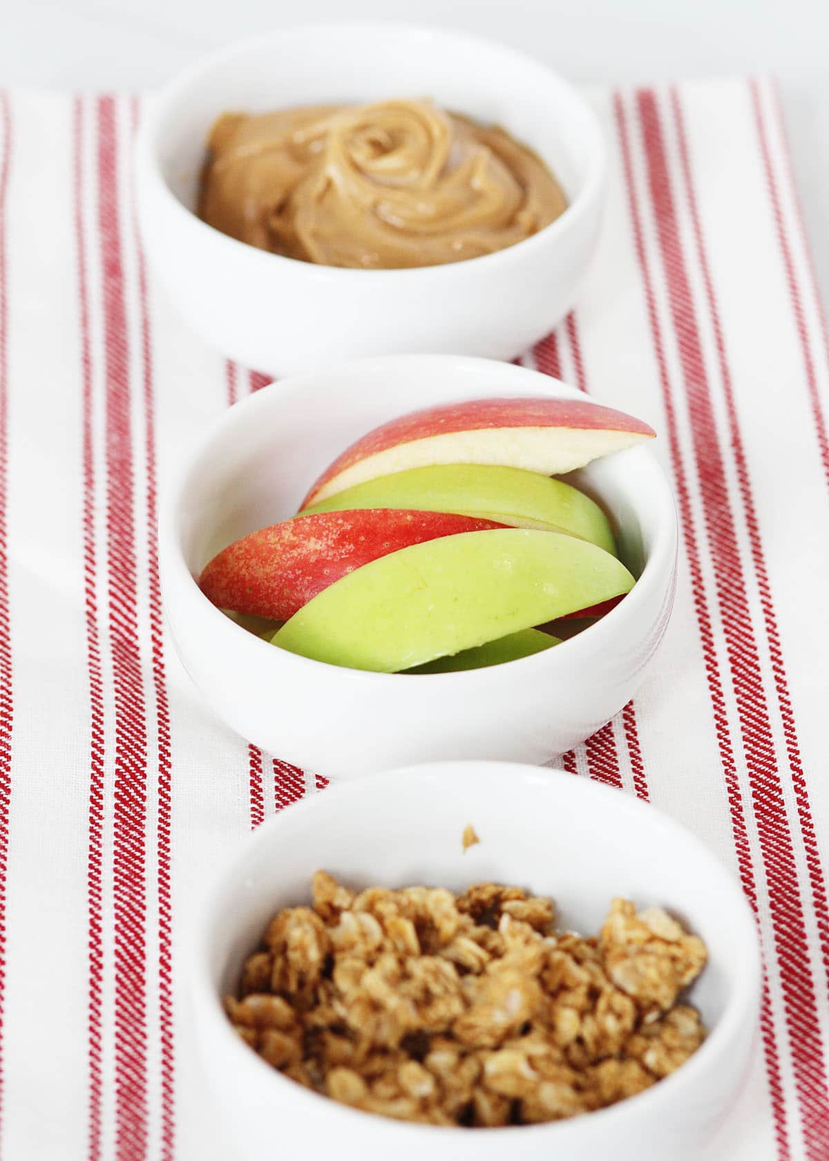 apple slices with granola and peanut butter in bowls to make an apple wedge snack