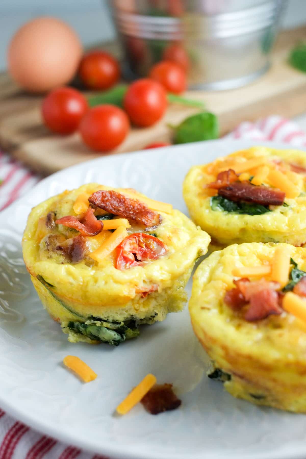 BLT Egg Muffin Cups 2 egg muffin cups with tomatoes, bacon and spinach on a white plate