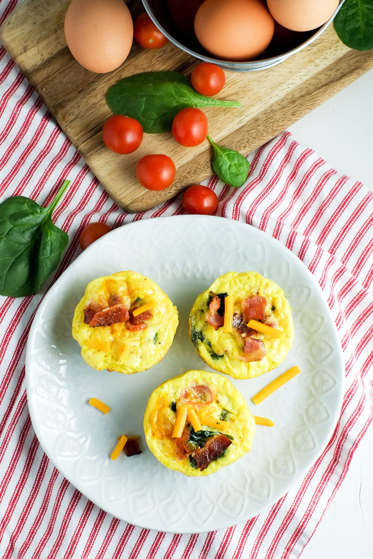BLT Egg Muffin Cups 4 cherry tomatoes, spinach and egg muffin cups on a white plate with a red and white striped napkin underneath