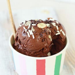 chocolate banana ice cream in a striped paper cup with a wooden spoon