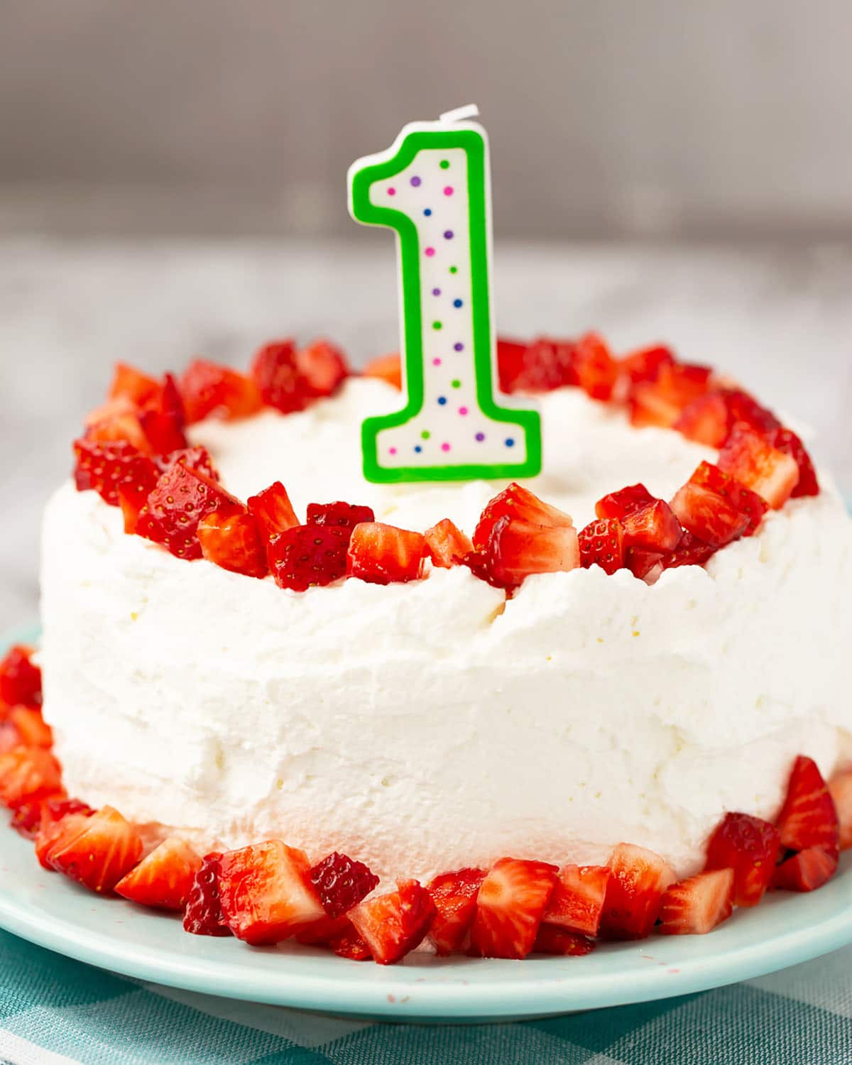 closeup of baby's first birthday smash cake with strawberries on a blue plate