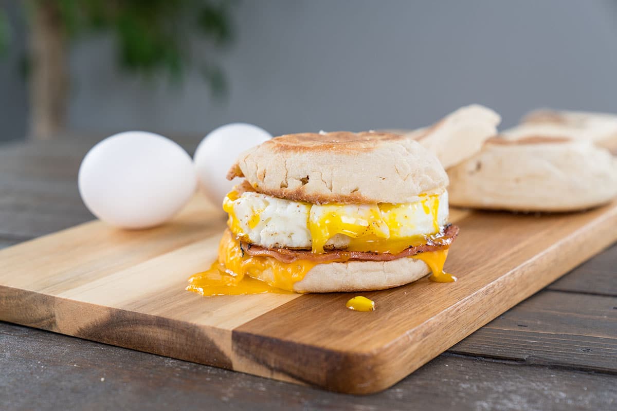 Canadian Bacon, egg and cheese breakfast sandwich with english muffin on cutting board with running yoke