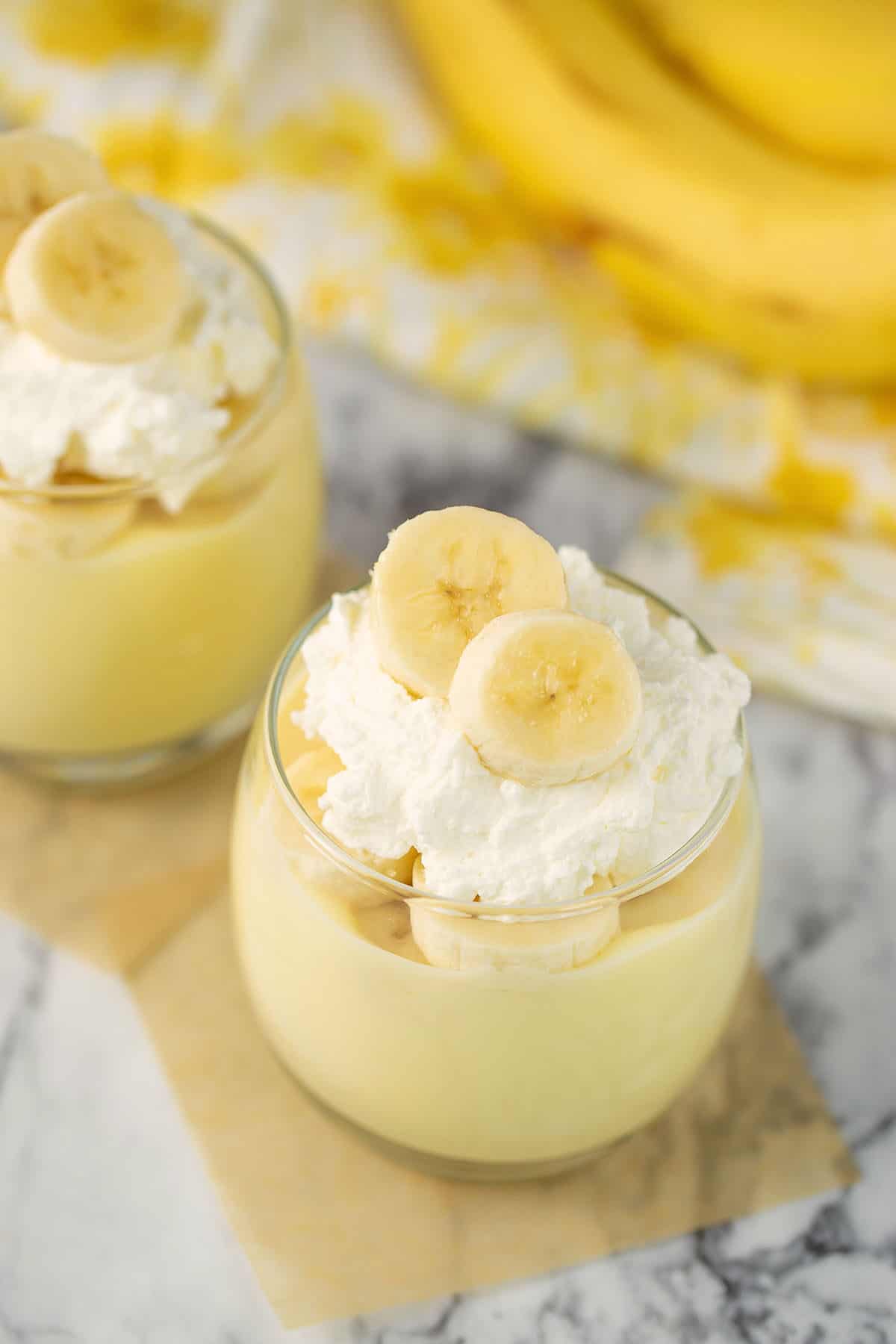 homemade banana pudding with fresh bananas and whip cream on top in clear glasses