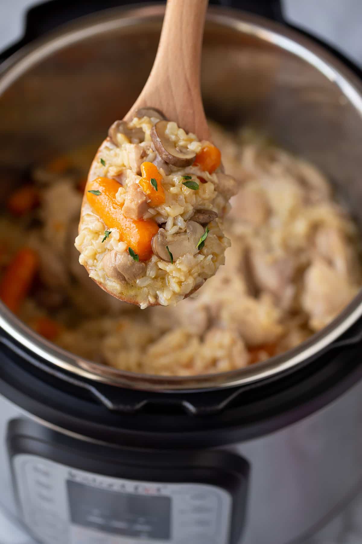 instant pot chicken and brown rice with carrots, mushrooms, rice and chicken on a wooden spoon above the instant pot