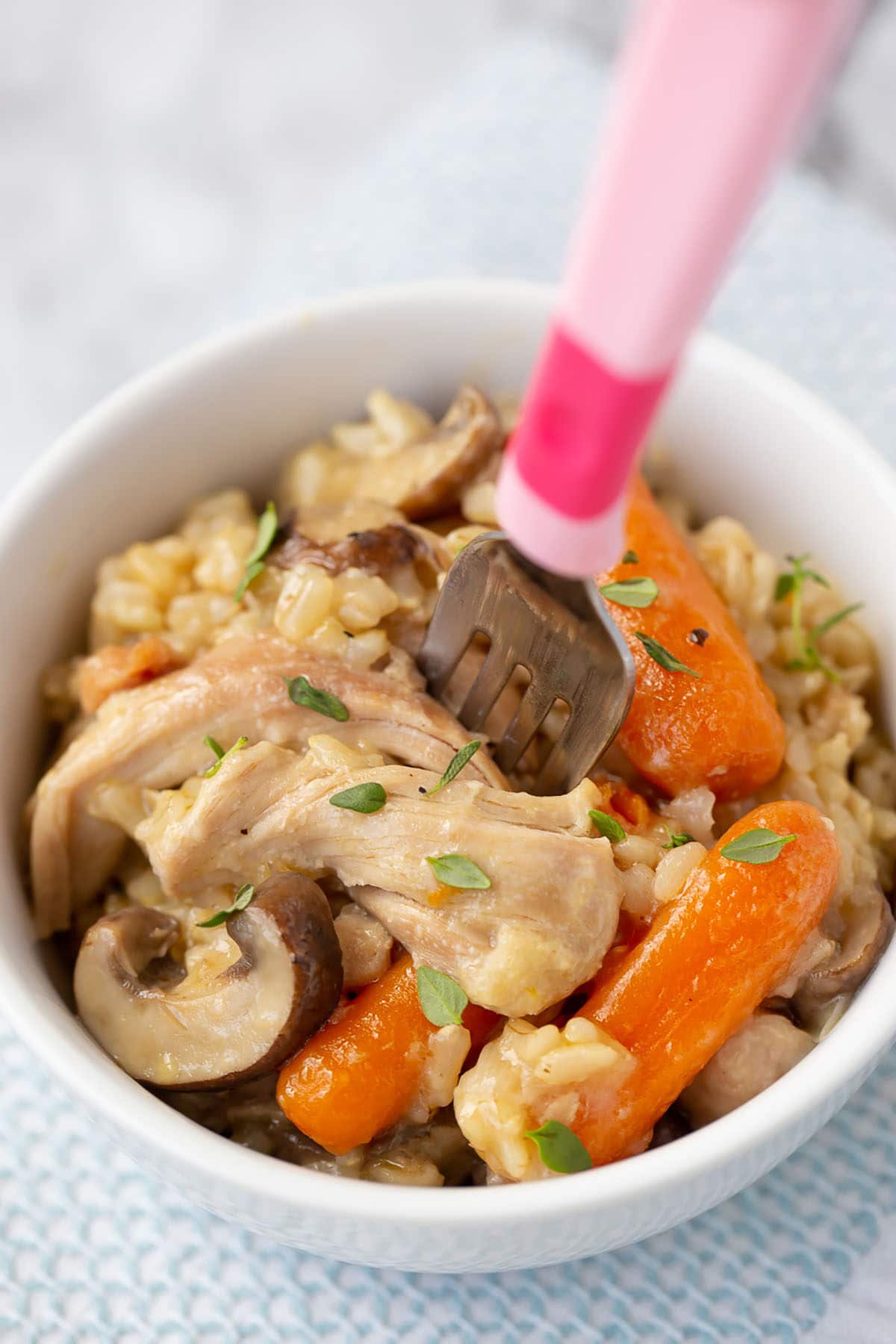 instant pot chicken and brown rice with chicken, mushrooms, carrots and brown rice in a white bowl with a pink fork